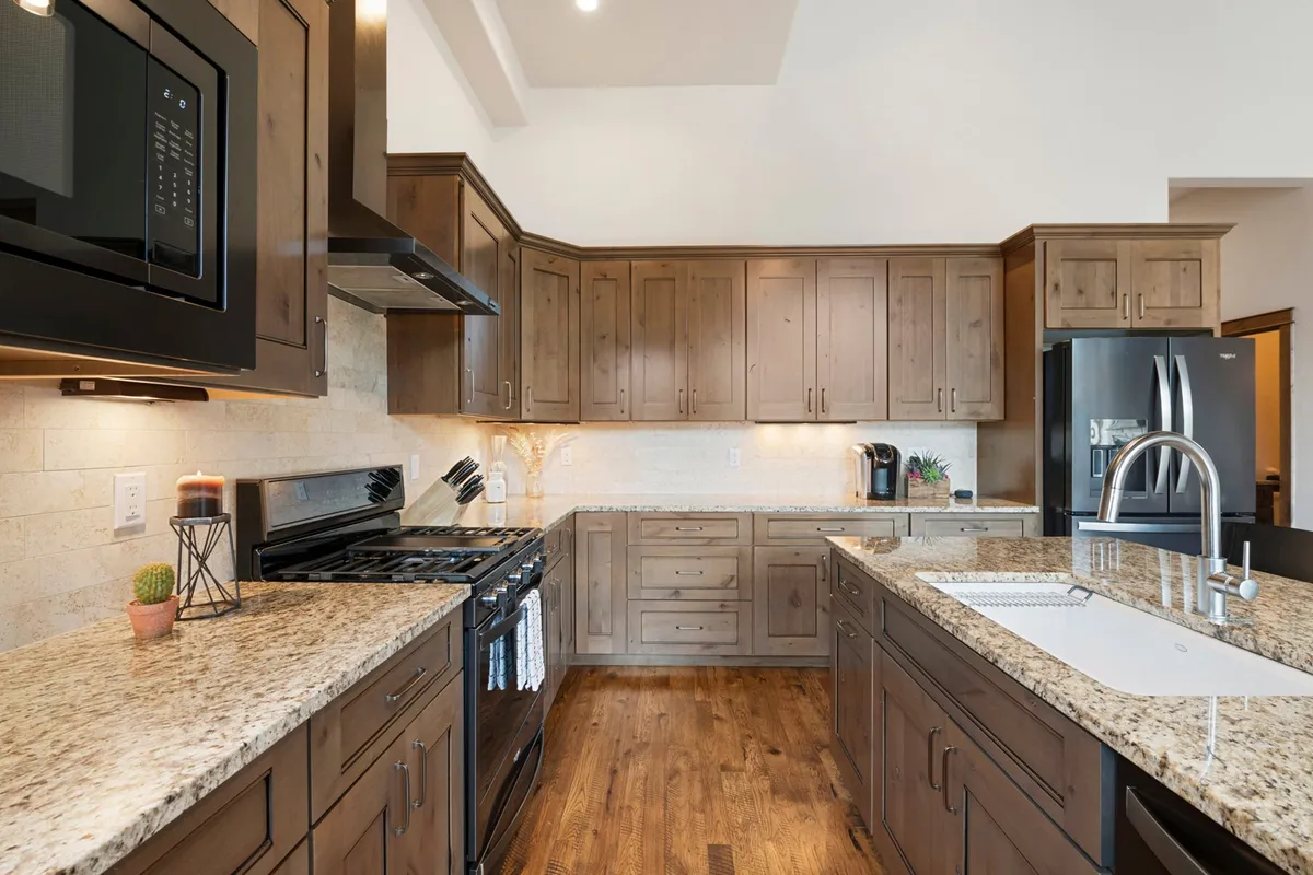 A spacious kitchen area with granite countertops, wood cabinetry, stainless steel appliances, and a central island that encourages family gatherings and culinary adventures. The warm, inviting lighting creates a sense of home and hospitality.