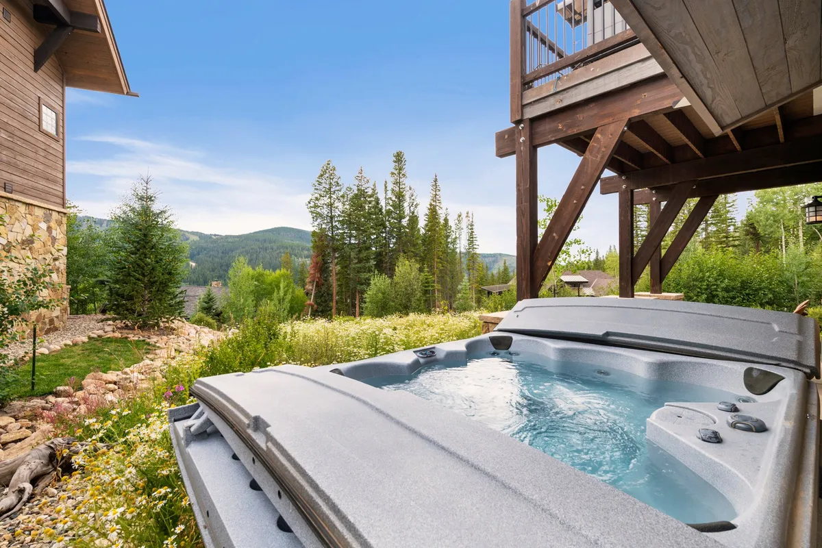 A serene exterior view of a private hot tub set on a deck, surrounded by lush greenery and overlooking sweeping mountain vistas. The inviting jacuzzi is perfectly positioned for soaking in the scenery, with plenty of space for relaxation and socializing.