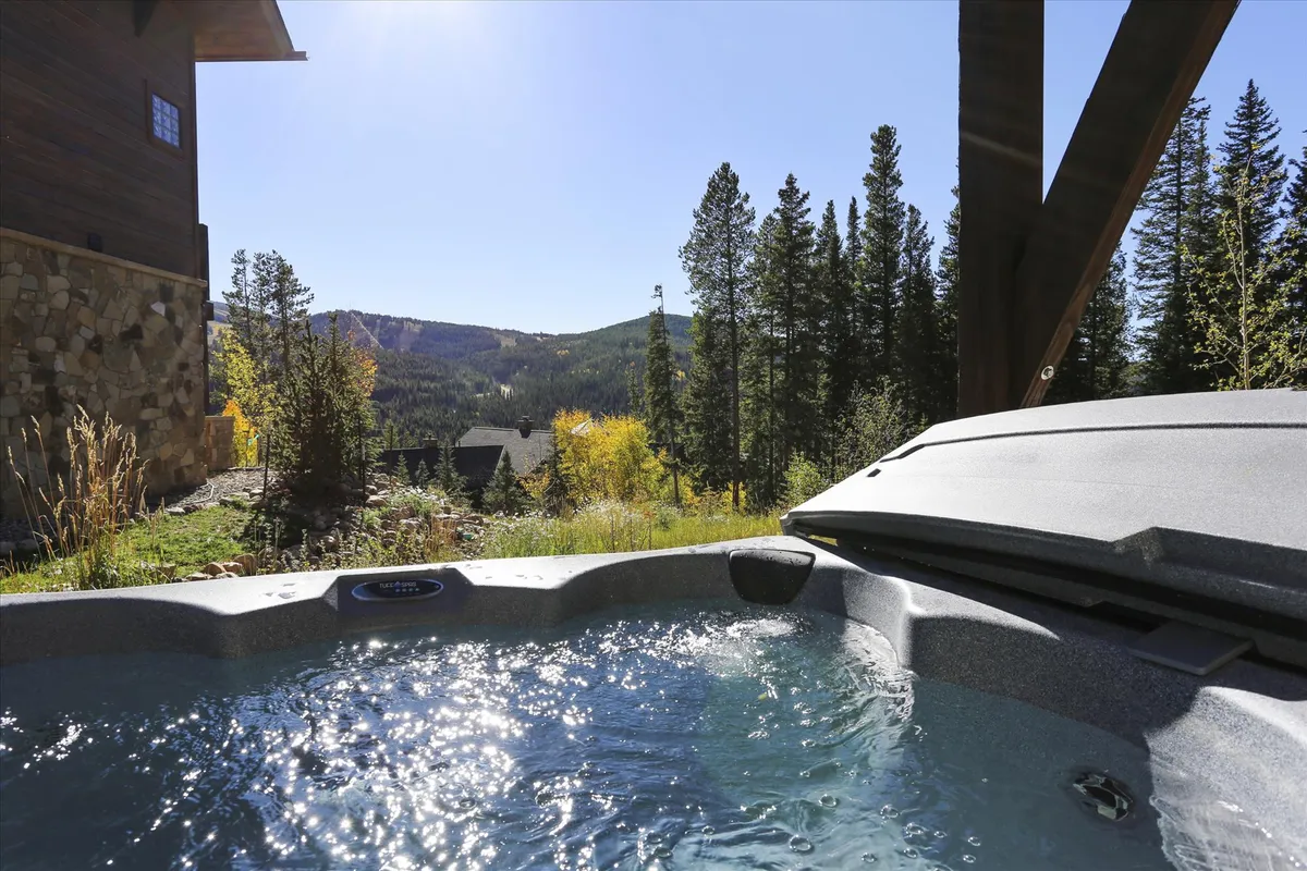 This exterior image showcases a private hot tub surrounded by lush greenery and overlooking breathtaking mountain vistas. The hot tub is the visual focal point, with surrounding trees and open sky creating a tranquil, secluded atmosphere ideal for relaxation after adventure-filled days.