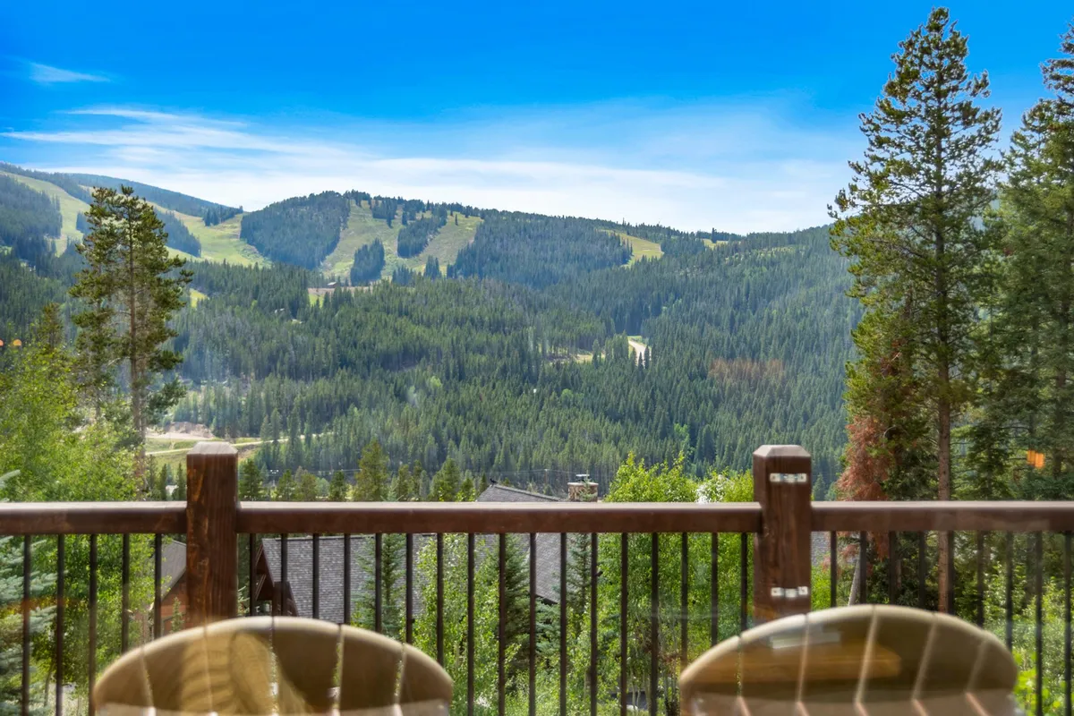 A peaceful deck with a railing overlooking sweeping mountain views, surrounded by trees. The setting is tranquil, with sunrise casting golden light over the landscape. The deck invites relaxation, inspiration, and direct immersion in the Rockies' natural beauty.