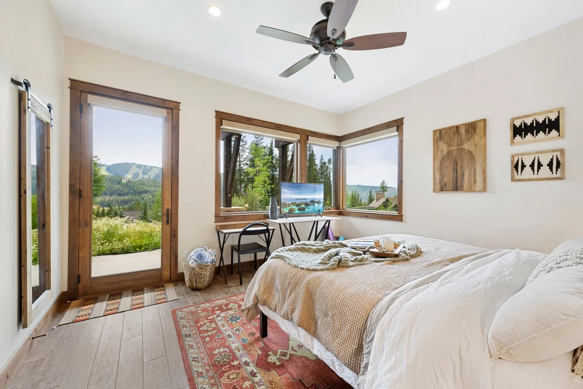 A serene king bedroom with soft, plush bedding, large windows framing a breathtaking mountain view, wooden furniture, and tasteful artwork on the walls. The ambiance is peaceful and inviting, ideal for rest and rejuvenation.