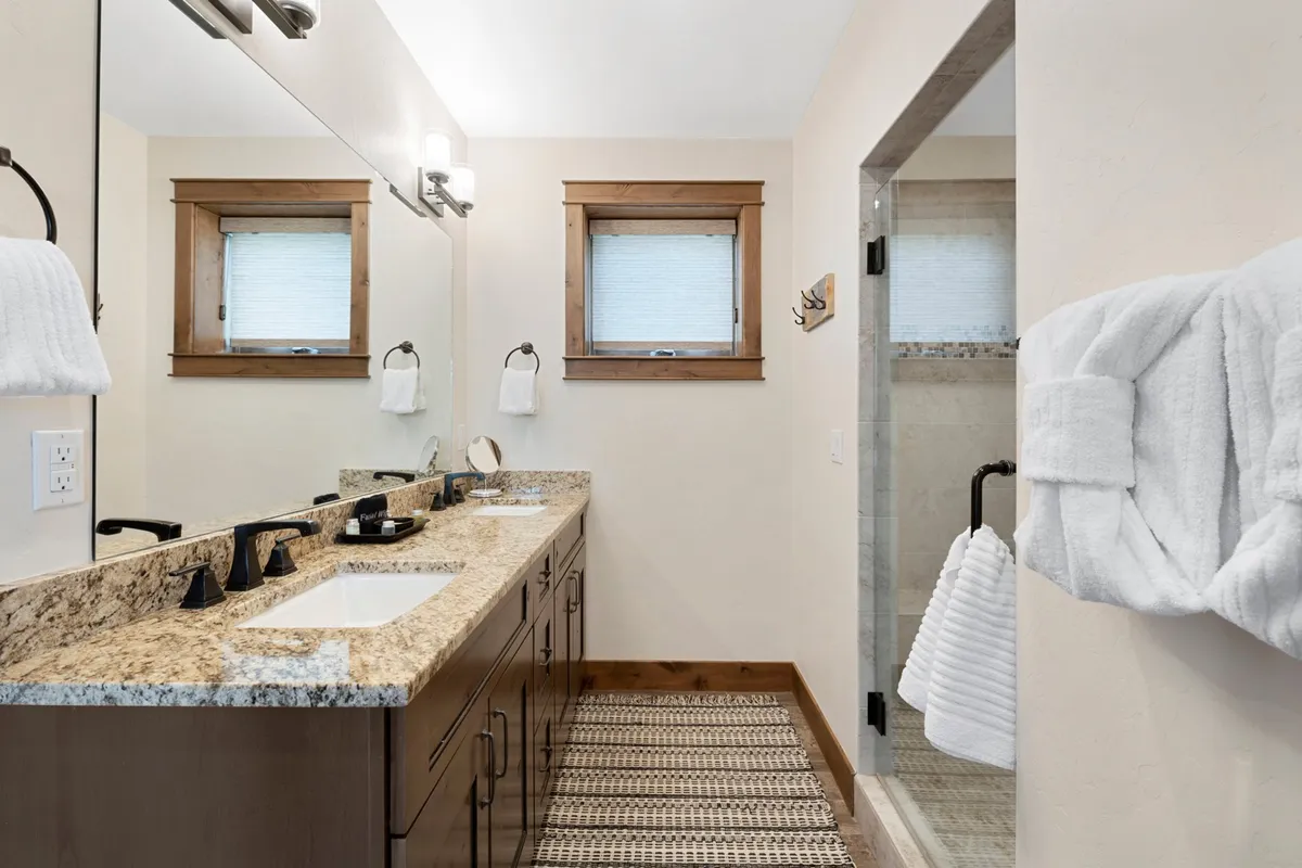 A modern ensuite bathroom featuring a double sink vanity, granite countertops, large mirrors, and a spacious shower area. The space feels calming and spa-like, ideal for personal grooming and self-care routines.