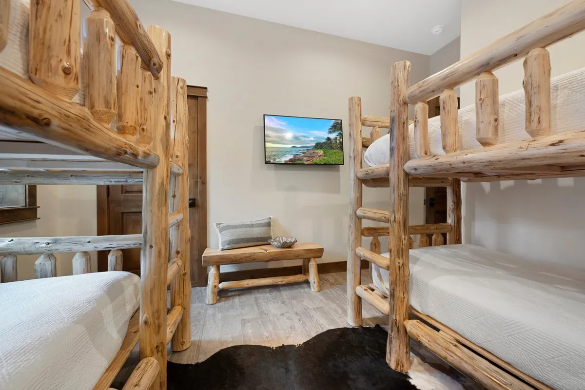 A guest bedroom with cozy bunk beds, a wooden bench, and a wall-mounted TV, designed to accommodate multiple kids or friends. The inviting setup encourages relaxation and group activities, making it perfect for families or groups.