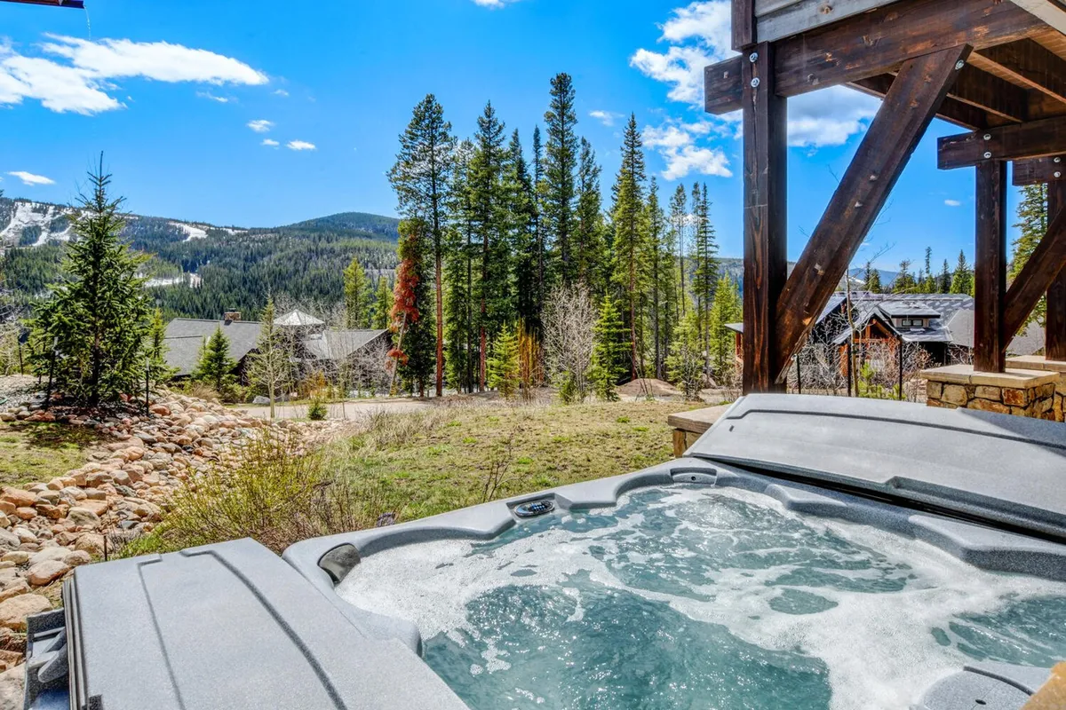 An inviting hot tub set amidst mountain views, pine trees, and residential villas, with guests relaxing in the soothing water at sunset. The tranquil atmosphere hints at the perfect retreat after a day filled with outdoor excitement.
