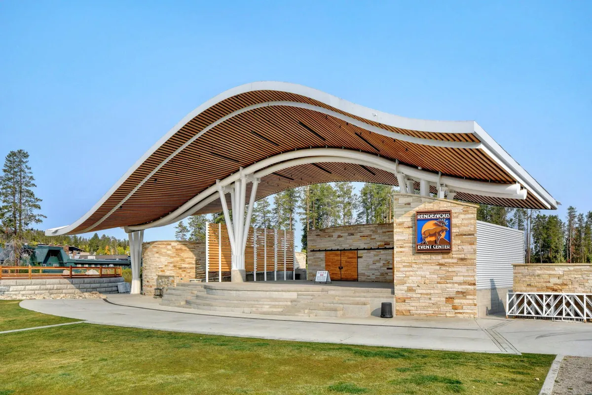 An inviting exterior shot of an event center with a curved roof, stone walls, and a clear event center sign. The setting is ideal for outdoor events, concerts, and community gatherings, reflecting a festive and communal atmosphere.